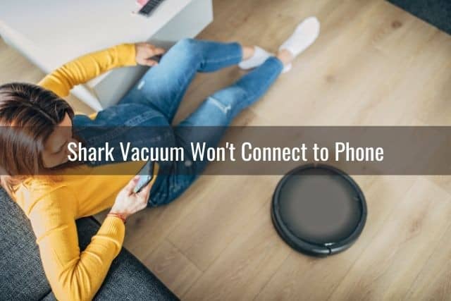 A lady sitting on the ground using her phone to control her robotic vacuum