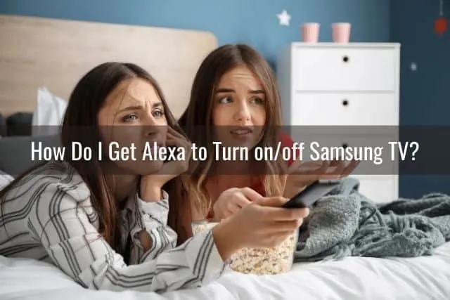 A couple of teenage girls lying on a bed frustrated with a TV remote control