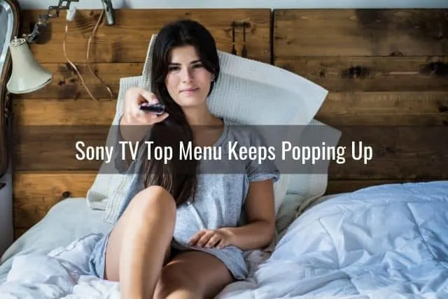 Female sitting on bed pointing remote at TV