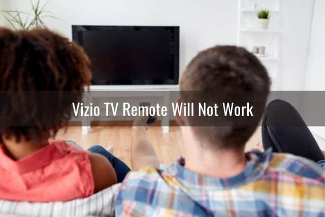 Couple sitting on sofa with male using remote to turn TV on