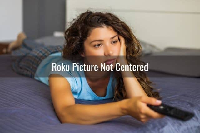Bored female on bed watching TV with remote in hand