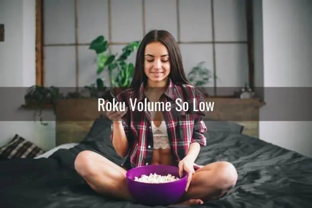 Young female sitting on bed with a bowl of popcorn and a TV remote