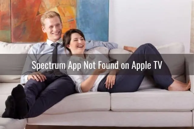 Male and female couple sitting on sofa laughing at TV programming