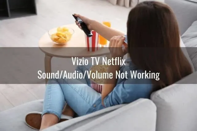 Female sitting on sofa eating popcorn and using remote to turn volume up
