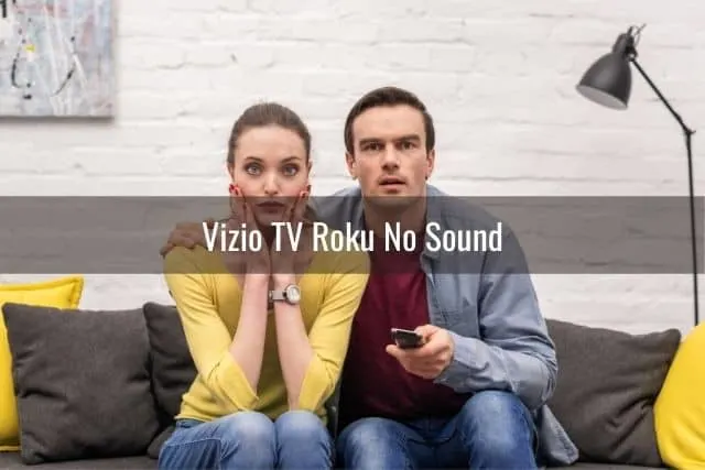 Male and female couple looking confused while watching TV on sofa